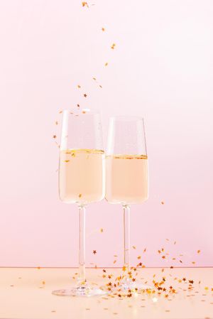 Two glasses of champagne and falling confetti stars on pink background