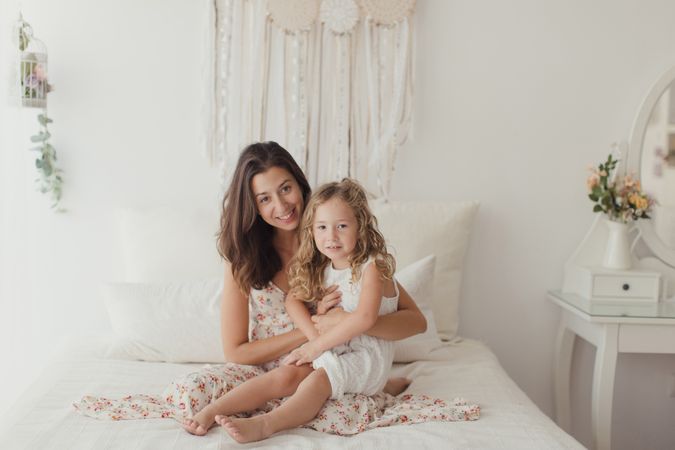 Mother ticking little daughter and laughing on bed