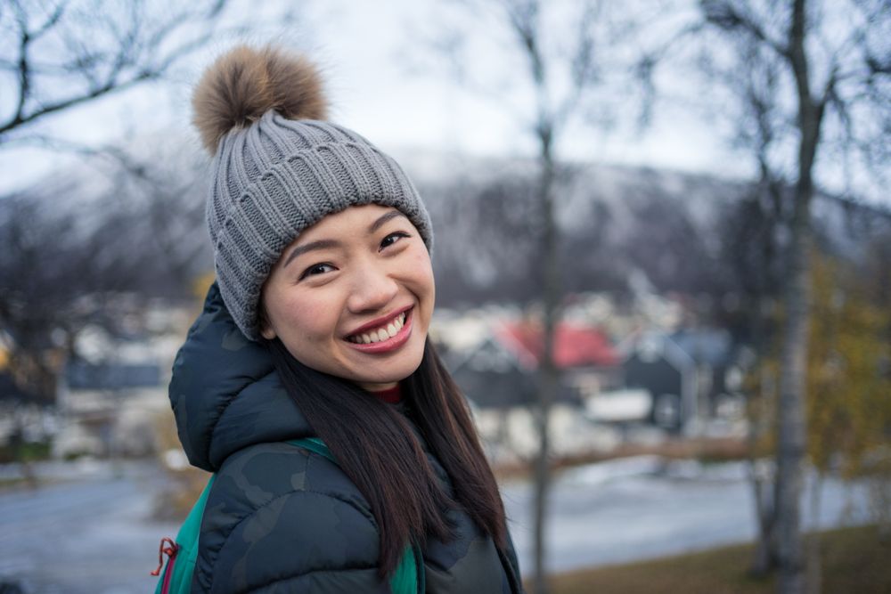Joyful Asian tourist on road bridge against modern building with unusual architecture at foothill in cold weather