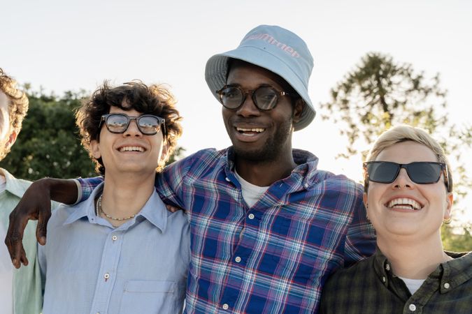 Diverse group of young friends smiling with arms around shoulders in outdoor summer light