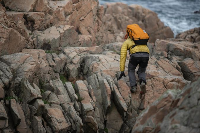 Man in yellow jacket and backpack climbing rocky mountain