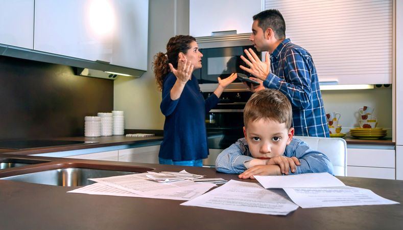 Couple arguing in front of little boy with bills strewn on the kitchen counter
