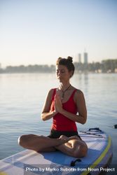 Woman peacefully meditating on paddleboard with her hands together 4Zlz10
