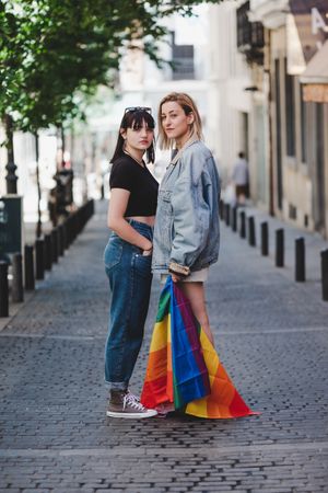 Lesbian couple with LGBT flag standing on street