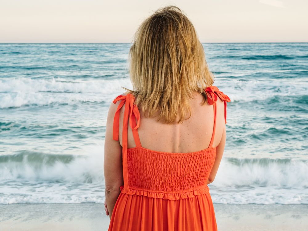 Woman in red dress looking along at seaside