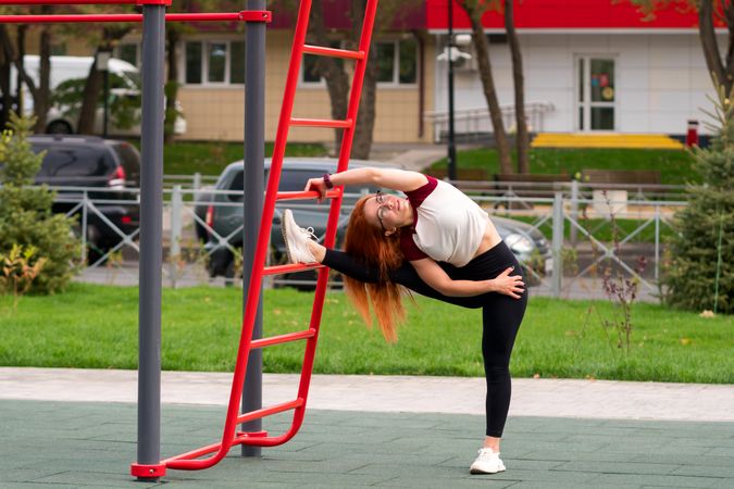 Woman performing side stretch on outdoor fitness equipment