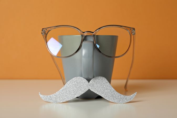 A cup with a mustache and glasses, on an orange background.