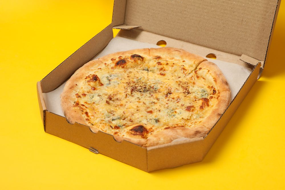 Cheese pizza in carton box on yellow background