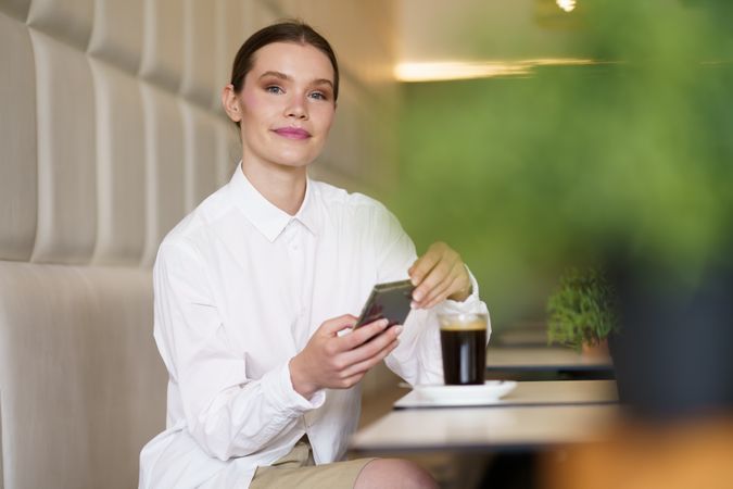 Successful elegant woman smiling while using smartphone in a cafeteria