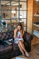 Busy businesswoman working with laptop talking on the phone sitting on the sofa