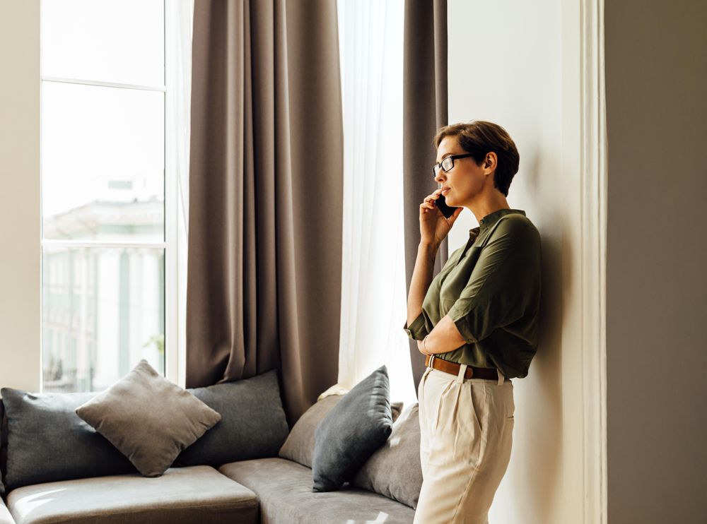 Woman leaning on wall next to a window taking listening to a phone call