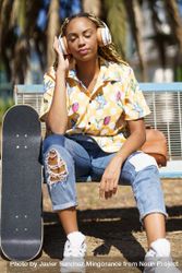 Female in bold patterned shirt sitting on park bench listening to music on large headphones 5ow3G5