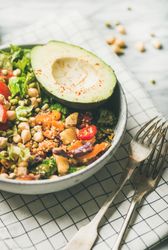 Close up of lunch bowl with avocado, sprouted grains, vegetables, with forks on checkered napkin