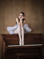 Positive ballerina sitting on piano in pointe shoes