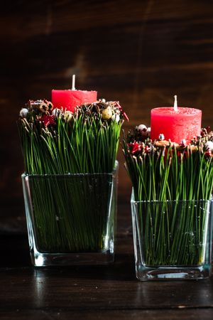 Side view of red Christmas candles and spice decor in vase on dark background