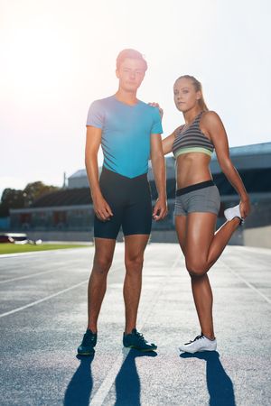 Full length shot of young man and woman standing on athletics race track