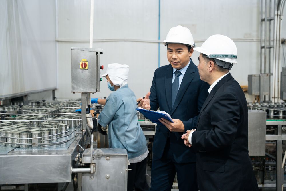 A businessman inspecting canned fish on conveyor belt at the factory