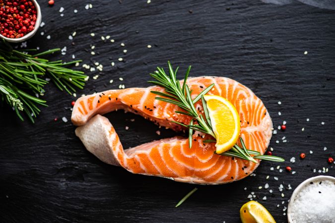 Looking down at salmon steak with rosemary and lemon on dark counter with copy space