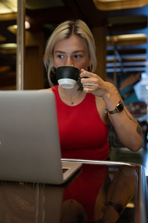 Blonde woman drinking coffee while working on her laptop