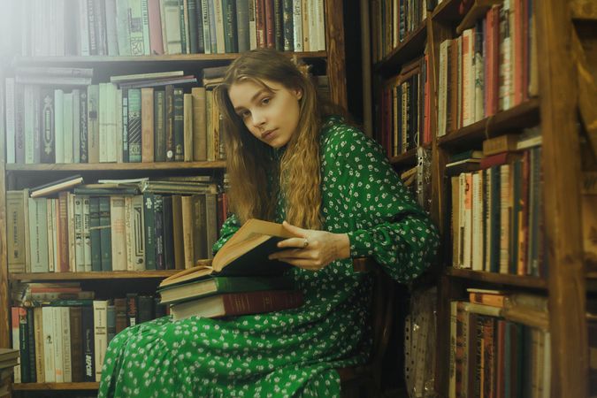 Portrait of girl opening a book while sitting beside bookshelves