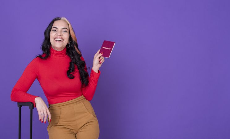 Young woman traveler with passport and suitcase against purple background.