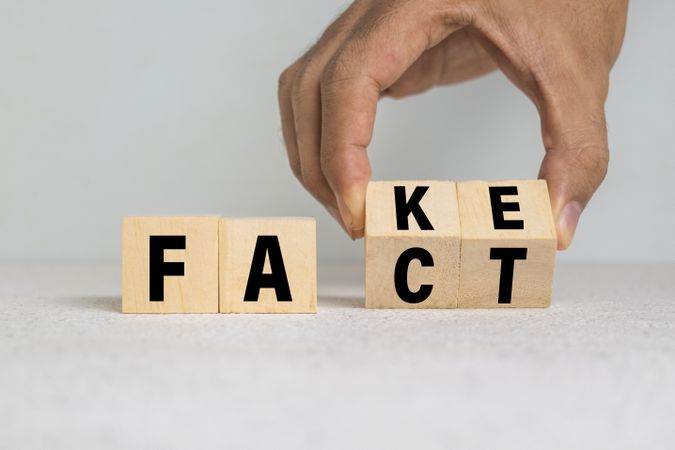 male hand flip wooden blocks with fake and fact words symbol on light background