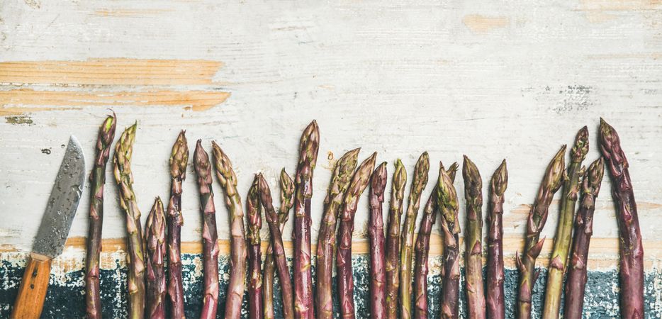 Lined up pieces of washed purple asparagus tips, on wooden board with copy space