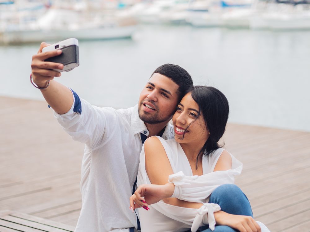 Woman with man taking photo selfie and kissing on bench