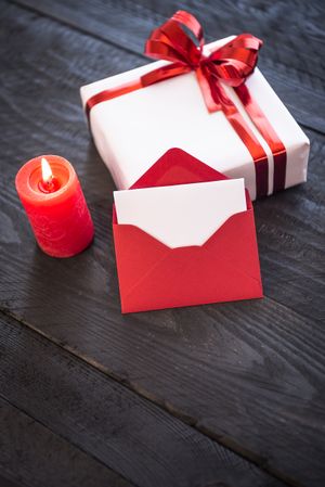 Candle, envelope and present on wooden table, vertical