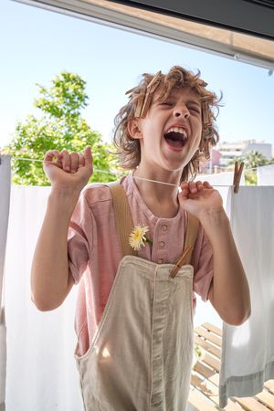 Funny child with clothespins in hair catching rope and screaming