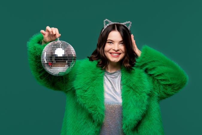 Smiling woman in green fur coat holds disco ball.