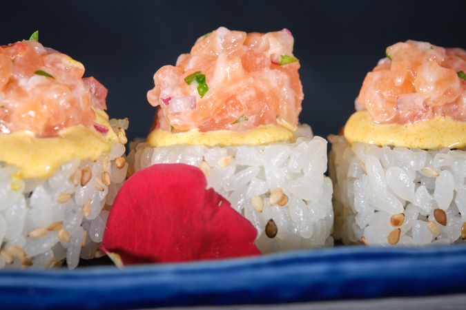 Appetizing sushi topped with salmon and fresh sauce served on blue tray