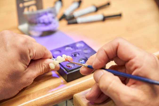 Faceless dental technician painting prosthesis
