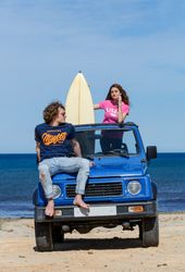Woman with surfboard and man sitting on car