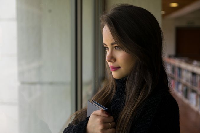 Woman with book looking out window