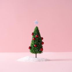 Christmas tree with red decorations with snow on pastel pink background