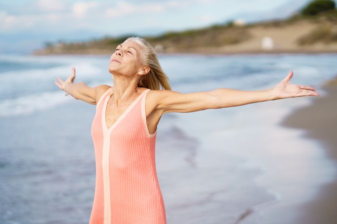 Carefree woman standing on the coast with her arms outstretched