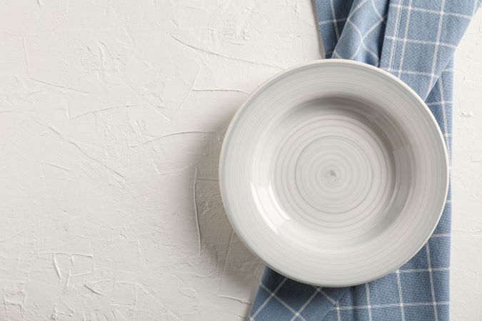 Kitchen towel with plate on light background, top view