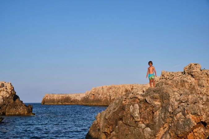 Boy standing on rock near blue sea