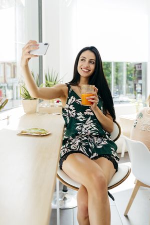 Woman with healthy drink taking selfie in cafe