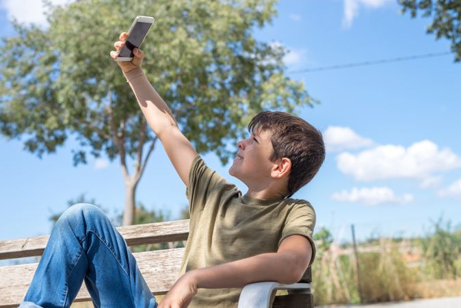 Boy sitting on bench taking selfie at phone