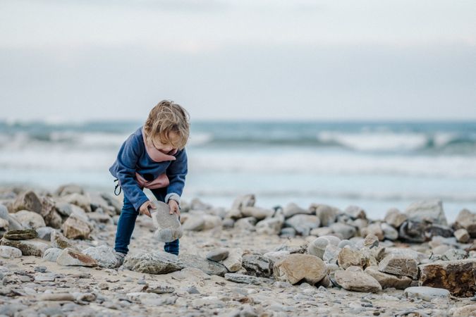 Smiling child near heap of stones on shore near water