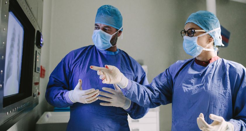 Two surgeons looking at screen and discussing while performing surgery in hospital operating room