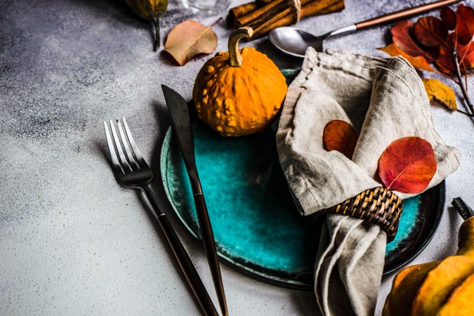 Fall table setting with colorful leaves, gourd and cinnamon sticks garnishing teal plate