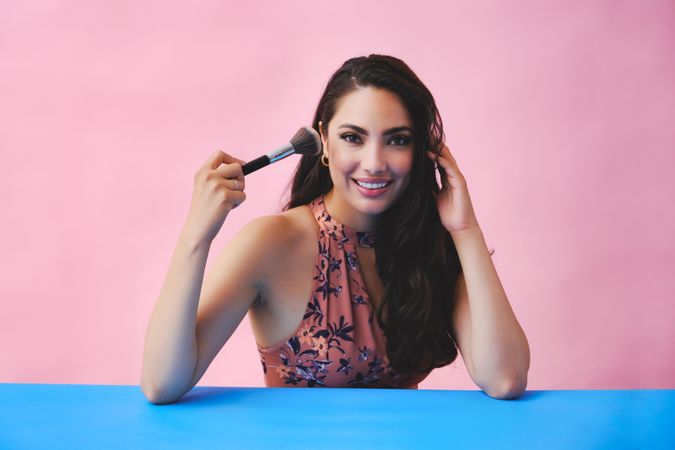 Elegant Hispanic woman with long brown hair holding large make up brush up to her face