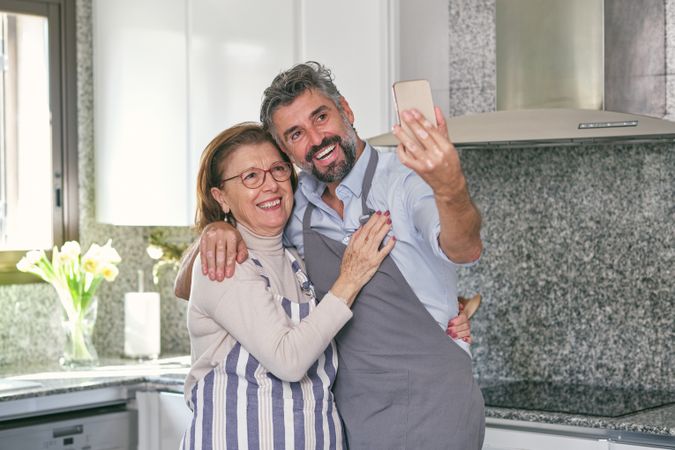 Happy woman and son taking selfie on smartphone in kitchen