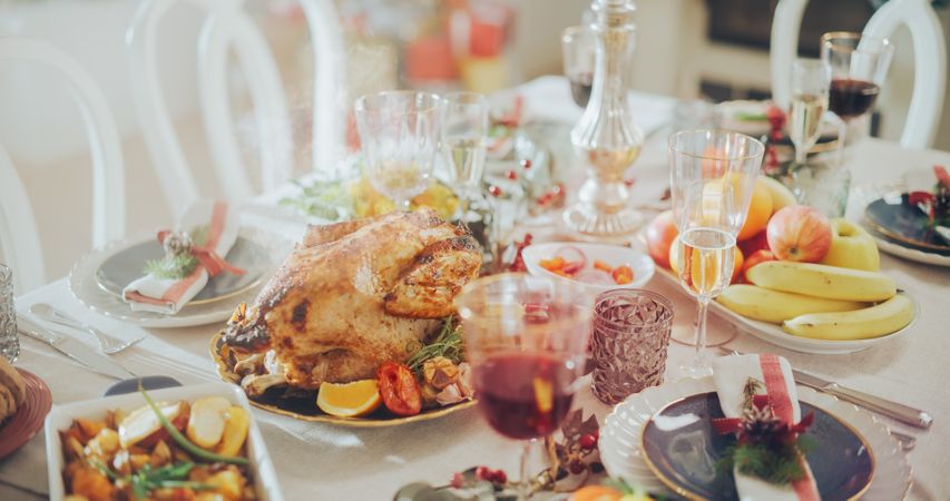 Tastefully Decorated Christmas Banquet Dining Table with a Grilled Chicken Dish, Vegetable and Fruit Garnishes, Baked Potatoes, Desserts and Drinks.