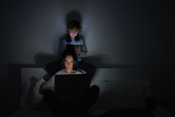 Positive woman and boy with laptop and tablet in bedroom at nigh