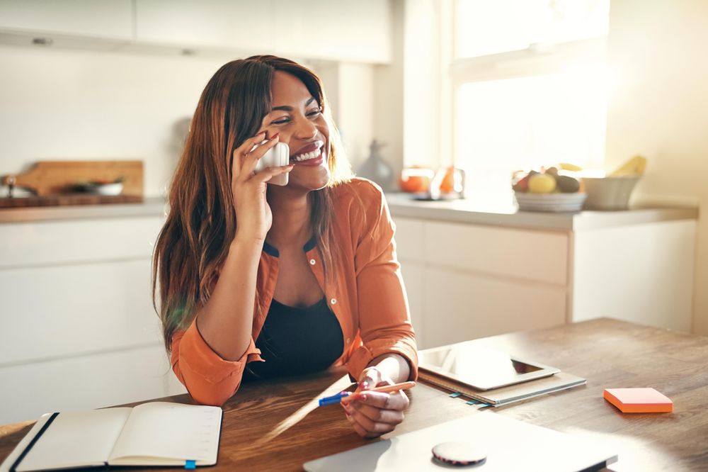 Businesswoman smiling while taking a call at her kitchen table