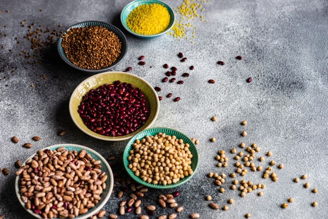 Variety of dried grains and legumes from pantry on grey counter with copy space